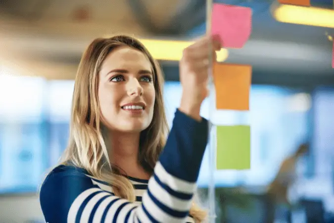 Woman smiling while planning and organizing sticky notes on a board.
