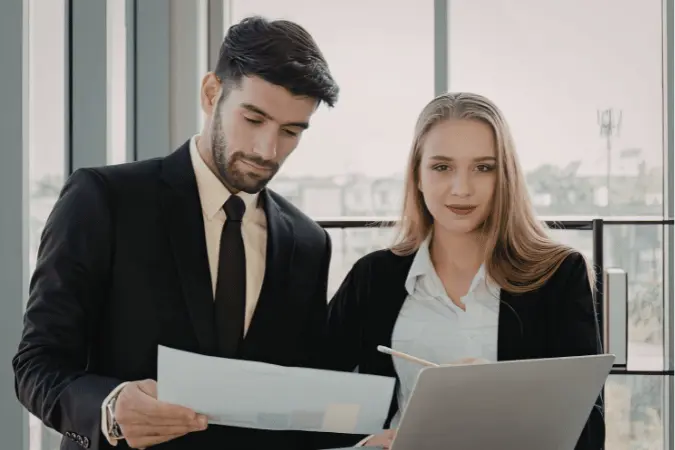 Two professionals reviewing qualification documents and a laptop together in a modern office