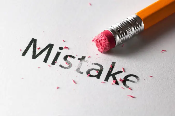 Pink pencil eraser removing the word 'Mistake' from white paper.