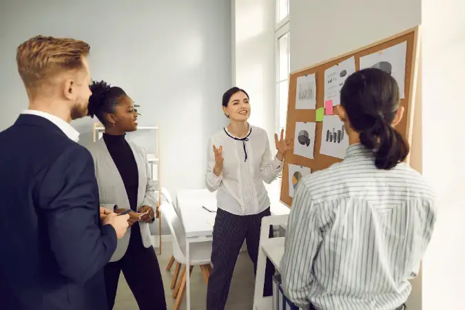 Sales trainer presenting to a team gathered around a board with charts and notes