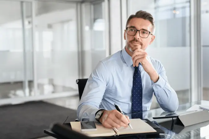 Professional man thoughtfully reviewing and writing documents at his desk
