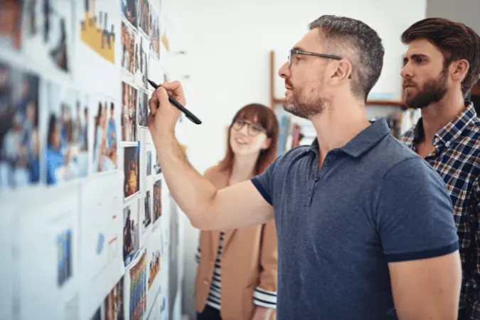 Three colleagues reviewing and discussing marketing plans on a wall board.