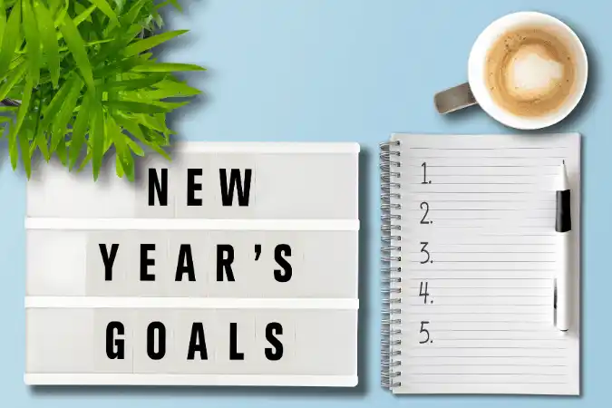 New Year's Goals sign next to a notebook, pen, and coffee cup