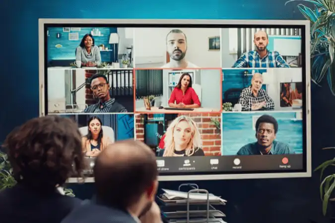 People viewing a video conference grid of diverse team members on a large screen.