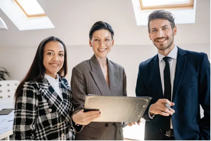 Three professionals in business attire discussing documents together in a bright office.