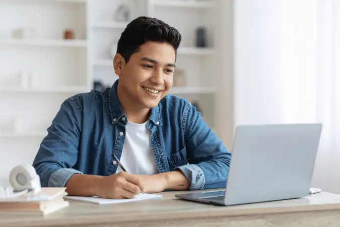 Man smiling while writing notes at his laptop, guide to the CIM Level 4 Certificate.