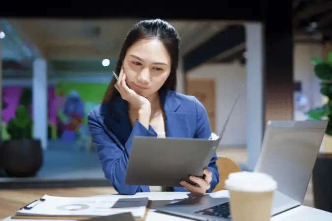 Woman thoughtfully reviewing charts next to her laptop, guide to the CIM Level 6 Diploma