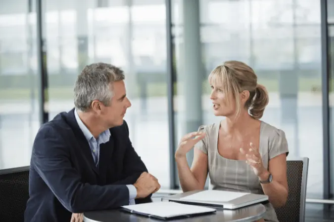 Two senior professionals discussing documents across a table in a bright office