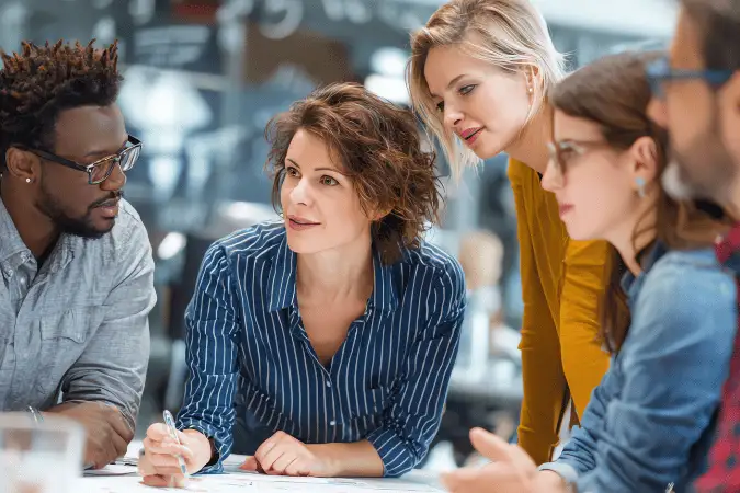 Five colleagues gathered closely around a table working through documents together.