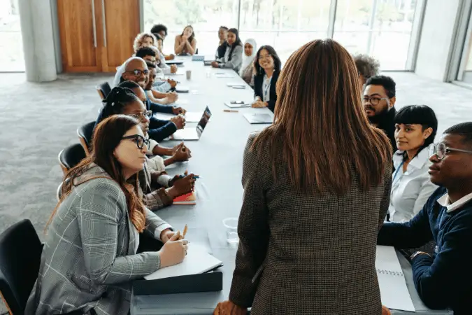 Leader addressing colleagues seated around a long boardroom table