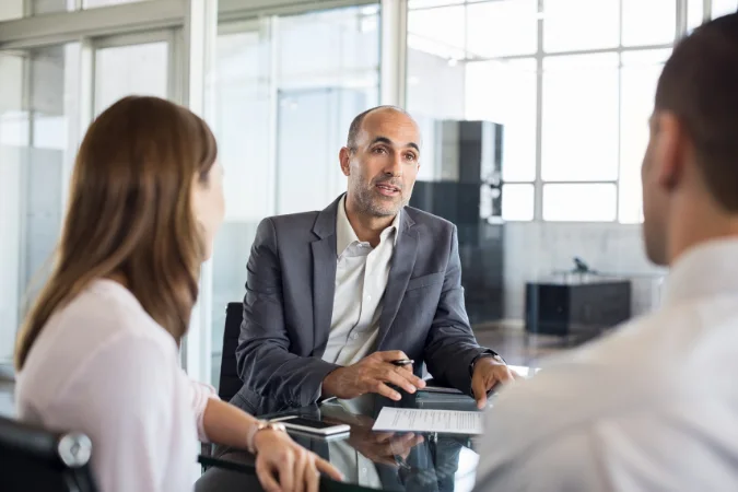 Adviser in conversation with two people across a table in a modern office