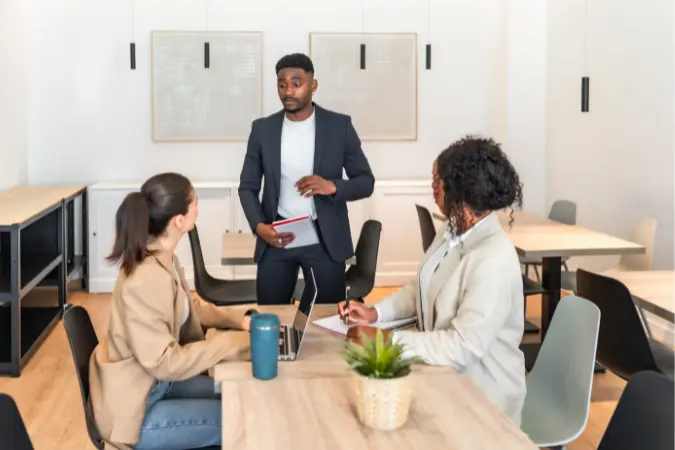 Manager standing and briefing two colleagues taking notes in a modern office.