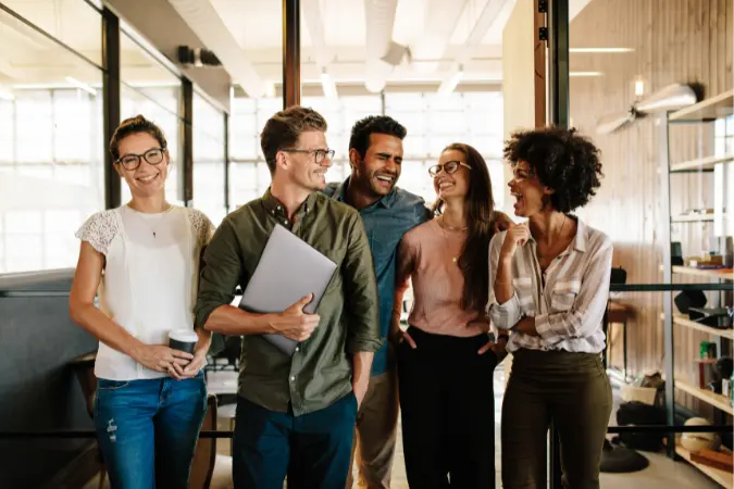 Five diverse colleagues walking together through a modern office, one carrying a laptop