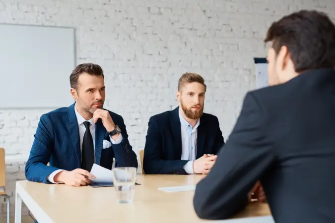 Two assessors listening to a candidate across a table during a professional discussion.