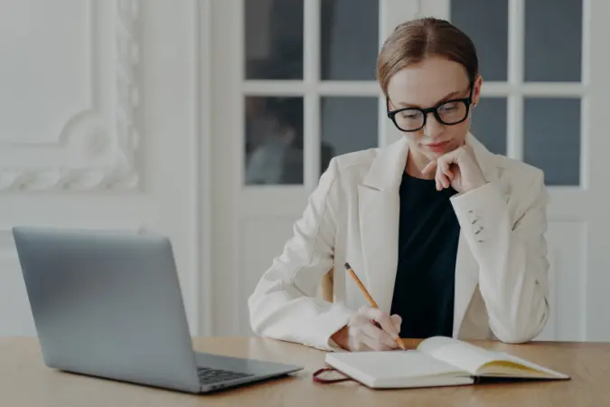 Professional writing plans in a notebook at her desk with a laptop open
