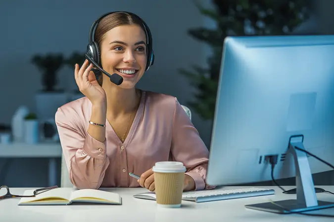 Customer service adviser wearing a headset smiling while taking a call at her desk.