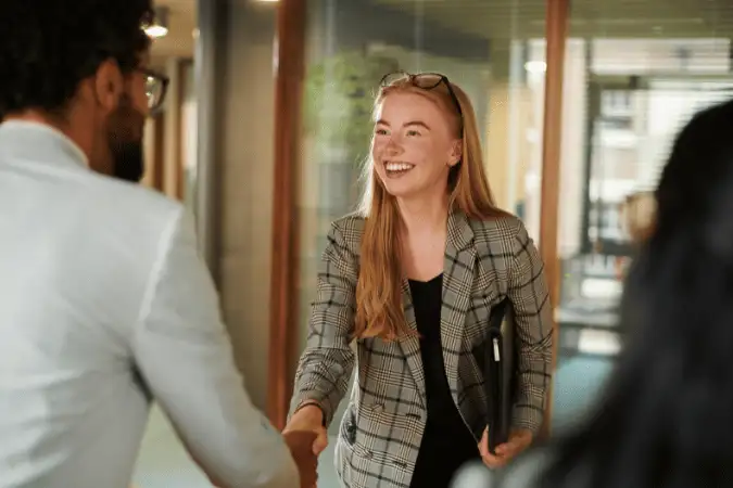 Young professional smiling at her desk with colleagues in the background.