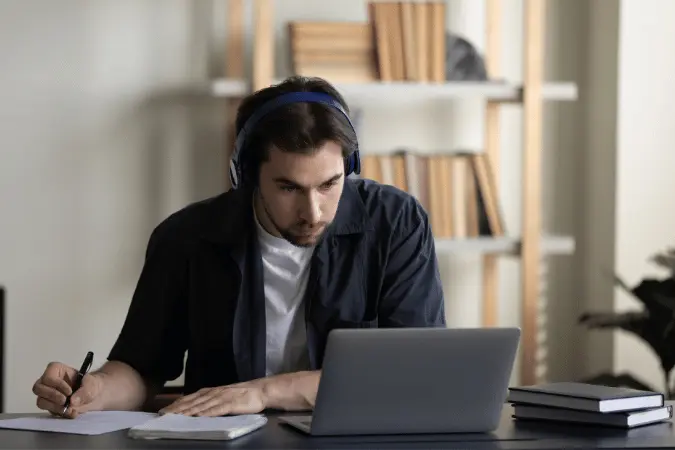 Man wearing headphones studying online course on laptop.