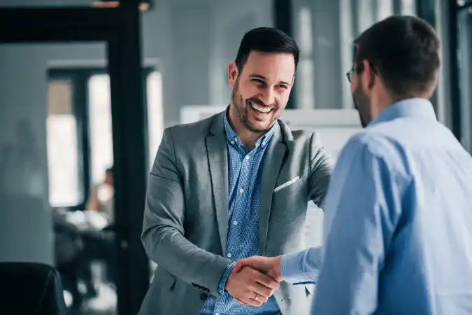 Two businessmen shaking hands and smiling in an office.