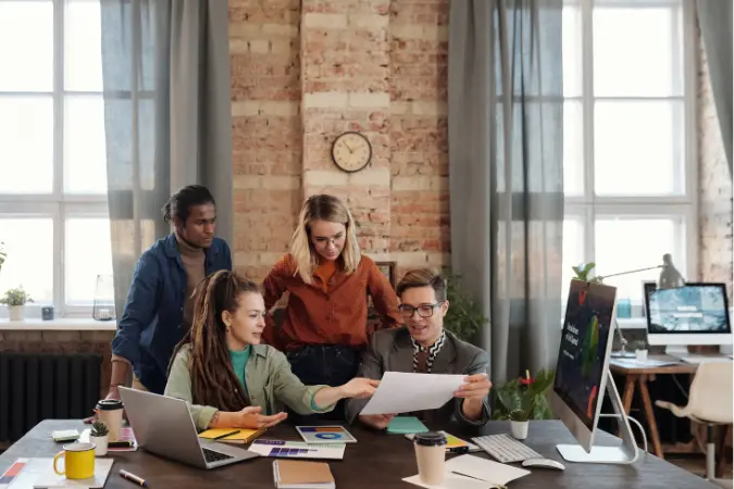 Group of colleagues gathered around a laptop reviewing work together in a loft office